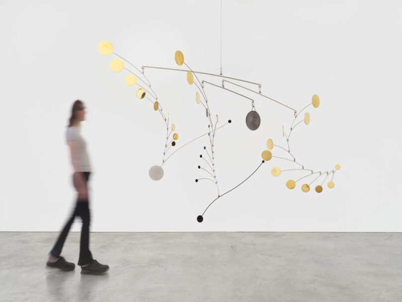 Person stands next to hanging brass sculpture of circles.