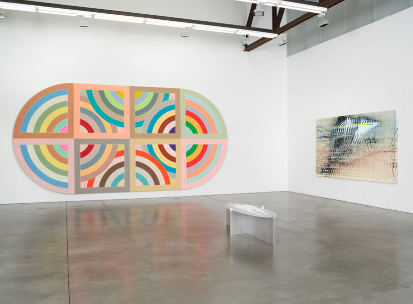 2 large colorful abstract paintings with small sculpture on floor.