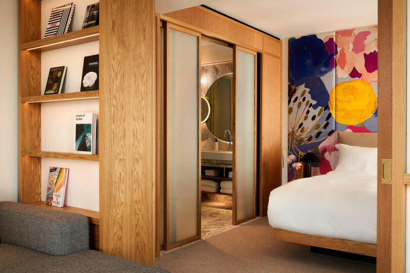 Experience the modern charm of BoTree Hotel's room, where a wooden sliding door elegantly separates the bedroom from the bathroom. The space features a cozy bed, shelves lined with books, and vibrant, abstract wall art that adds a splash of creativity to your stay.