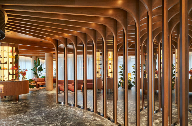 A modern interior space at BoTree Hotel features a series of curved wooden beams, marble flooring, and seating areas with plants and ambient lighting.