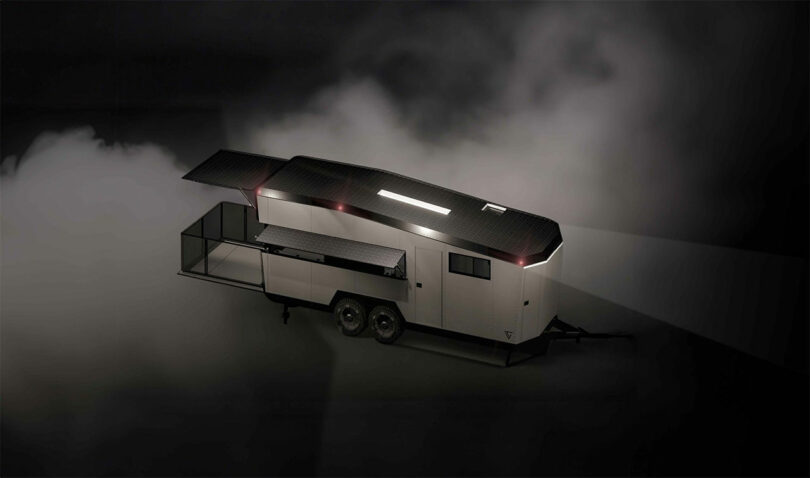 A sleek, modern CyberTrailer with extendable side panels is illuminated in a dark, foggy environment, showcasing its streamlined design and spacious interior.