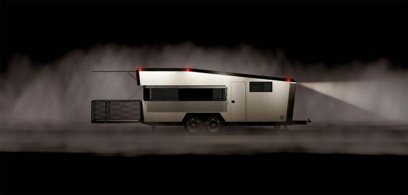 Side view of a modern, sleek CyberTrailer with a rear deck, illuminated by headlights in a dark, misty environment.
