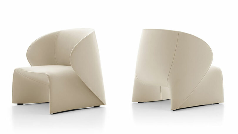 Two beige, modern, curved-back armchairs with smooth, minimalist design are shown against a white background. One chair faces forward and the other faces backward, displaying the full design from both angles.