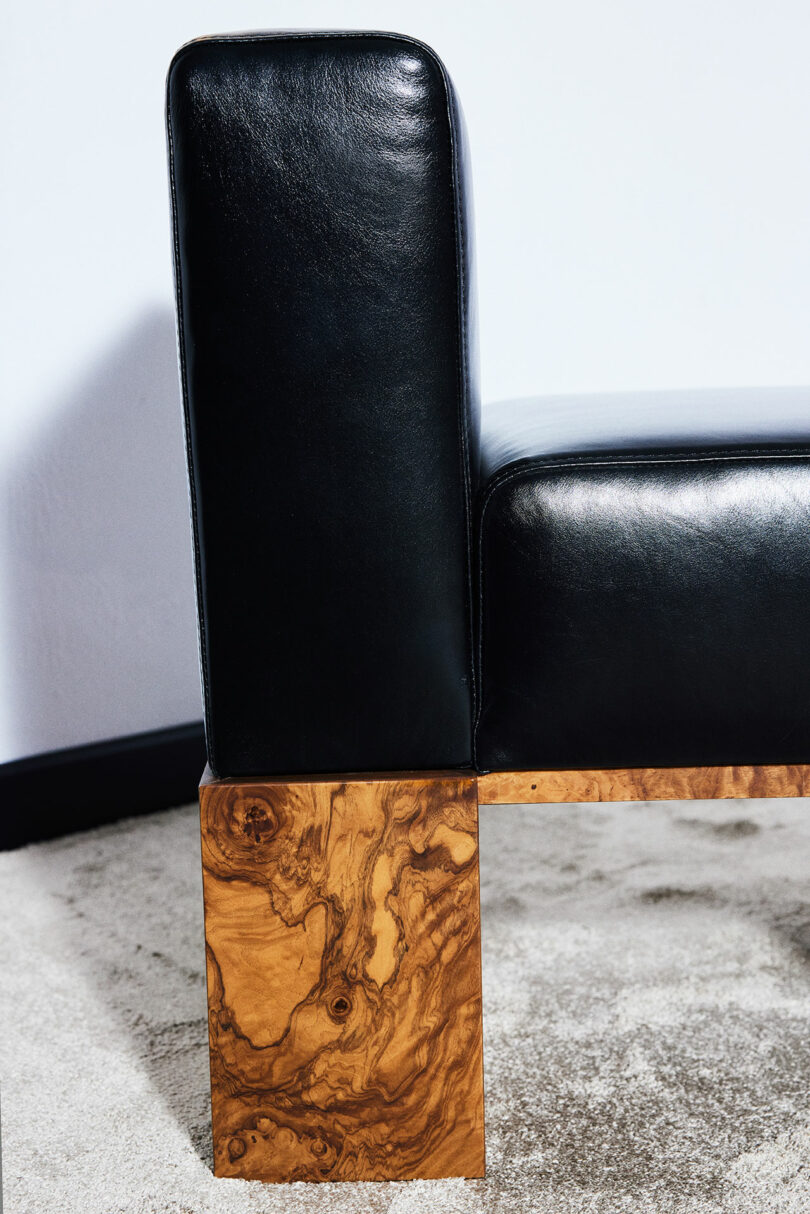 Close-up of a modern sofa featuring black leather upholstery and wooden legs with a distinctive grain pattern, placed on a beige carpet.