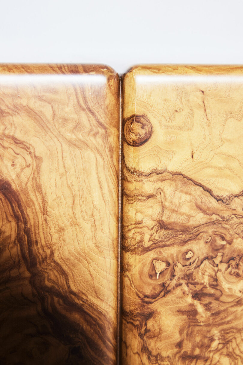 Close-up of a wooden surface with a natural grain pattern, showing two adjoining panels with distinctive swirls and knots in the wood.