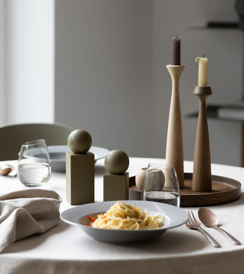 A round table with plates of pasta, two glasses of water, wooden salt and pepper shakers, and tapered candle holders