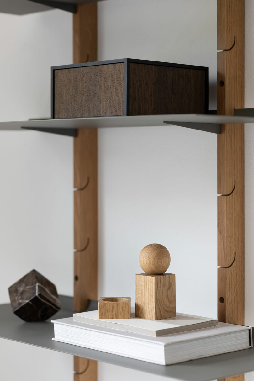 A wooden shelf unit with minimalist items including a wooden box, a wooden sculpture, and a white book displayed.