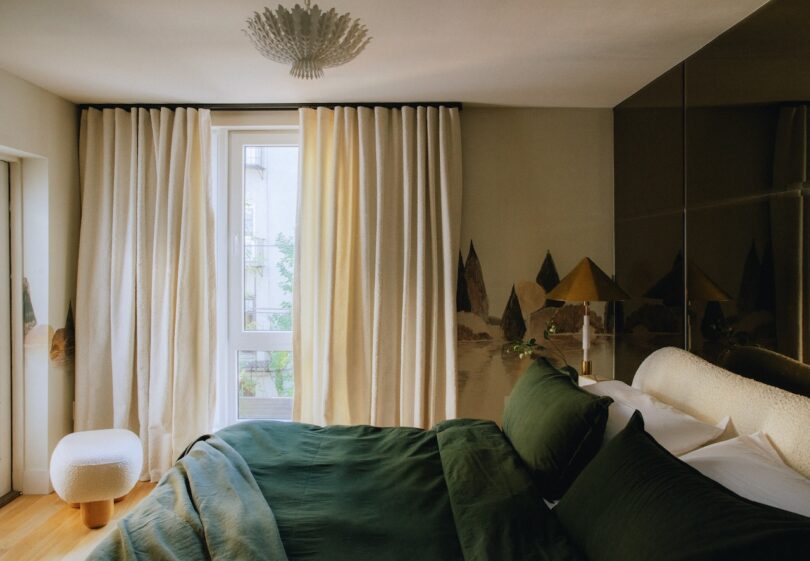 A cozy bedroom with a large window, white curtains, green bedding