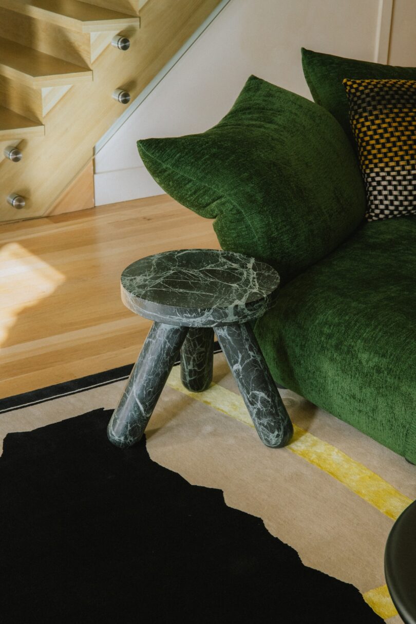 A green velvet sofa next to a unique marble side table