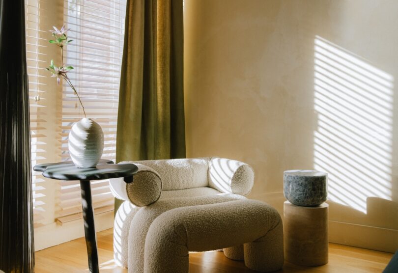 A cozy corner with a plush, curved armchair, a small side table with a vase