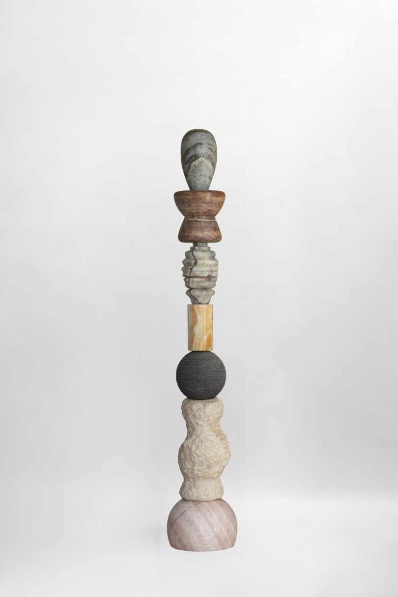 Full view of a totem sculpture from Sten Studio's "Cosmic Relics" collection, displaying a vertical arrangement of various stones, including brown, grey, golden, and black elements