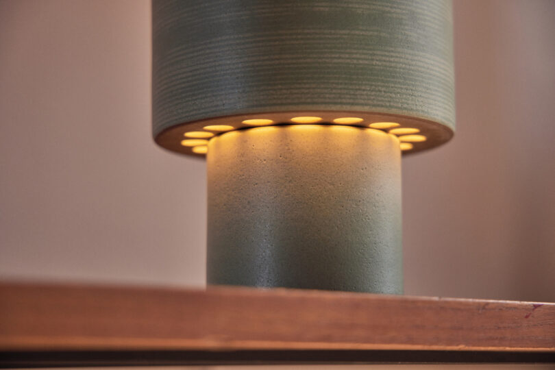 Close-up of a cylindrical lamp with a textured green surface, emitting a warm yellow light from its lower section