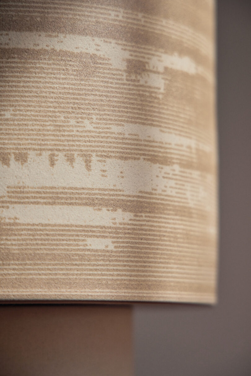 Close-up of a beige, textured lampshade, showing horizontal lines and a soft gradation effect with alternating rough and smooth patterns.