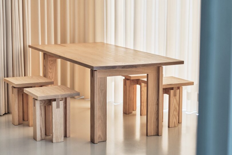 Minimalist wooden dining table with matching benches set in a room with light-colored curtains