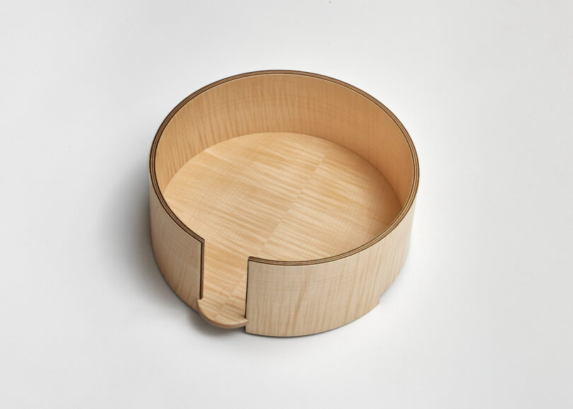 A circular wooden box with a vertical slot on one side, set against a plain white background.