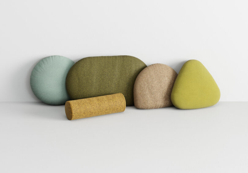 five variously shaped cushions in shades of green, beige, and yellow, arranged on a white surface