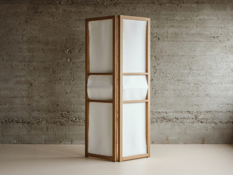 a paper and wood room divider in a room with concrete walls 