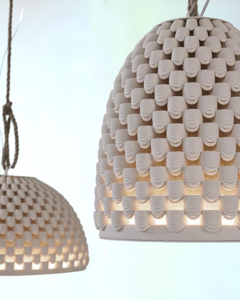 Close-up of two textured, dome-shaped hanging lamps with a honeycomb-like pattern, illuminated from within against a soft blue background