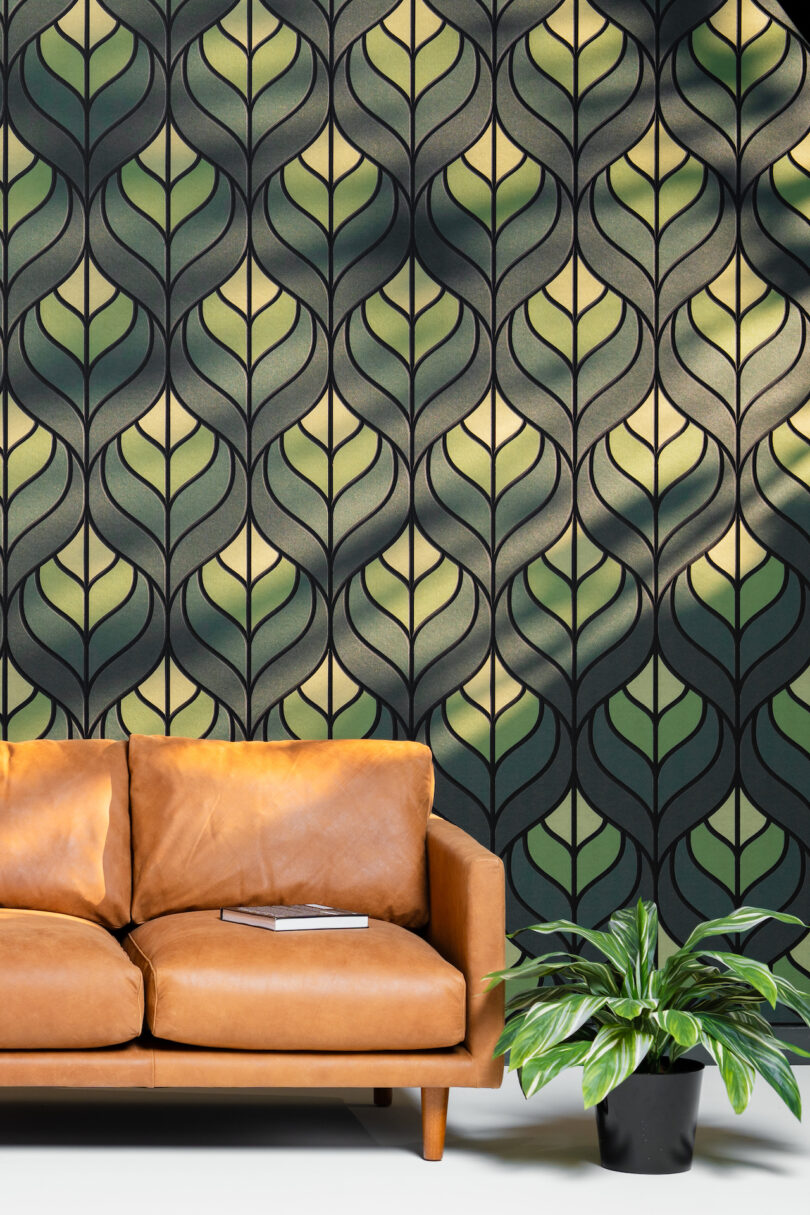 Brown leather couch on wooden legs next to a green potted plant in front of a black and green leaf-patterned wallpaper, with a book on the couch