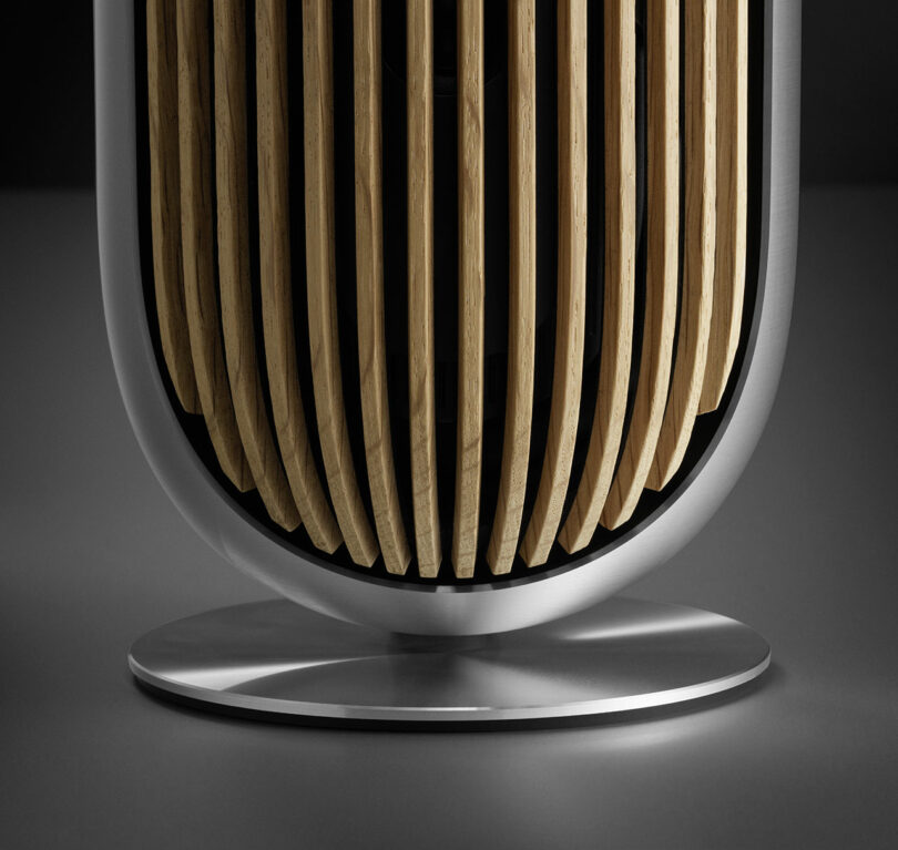 A close-up of the Beolab 8 speaker with vertical wooden slats and a metallic base.