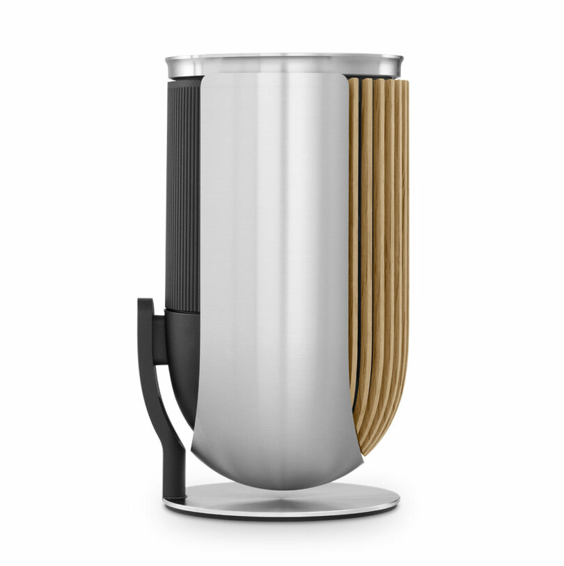 The Beolab 8 device boasts a cylindrical metallic body with vertical wooden slats on one side, complemented by a black segmented section and a curved metal stand.