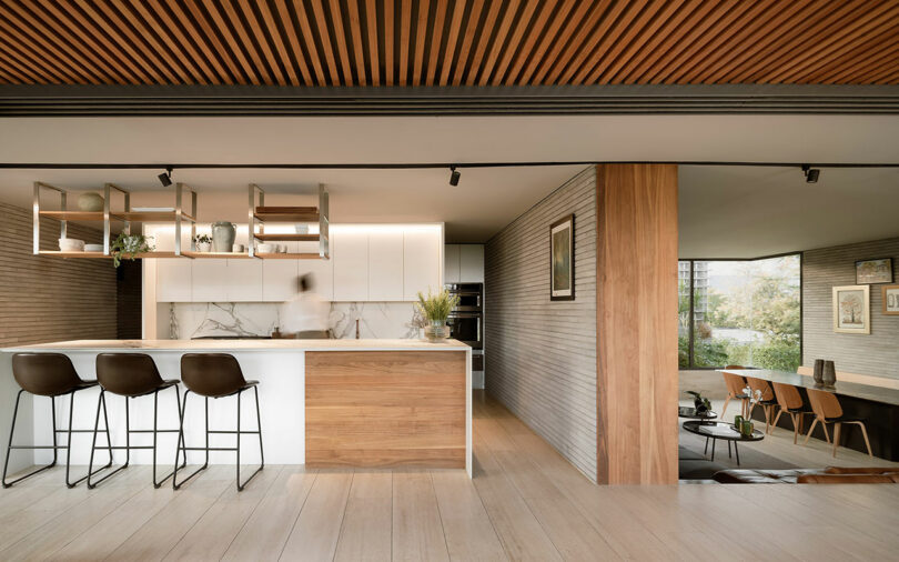 Modern kitchen and living area with neutral tones, wooden accents, and minimalist design. A person is blurred in motion near the sink.