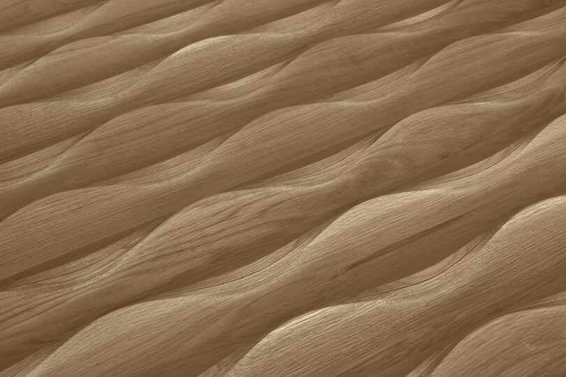 Close-up of a wooden surface with a wavy, undulating pattern, Design 406 by Erwin Hauer. The waves run diagonally across the image, creating a textured, three-dimensional appearance.