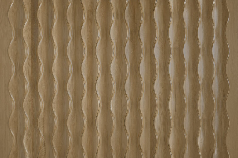 Close-up of a wooden surface, Design 406 by Erwin Hauer, with a wavy textured pattern consisting of vertical undulating lines. The wood has a natural, warm tone.