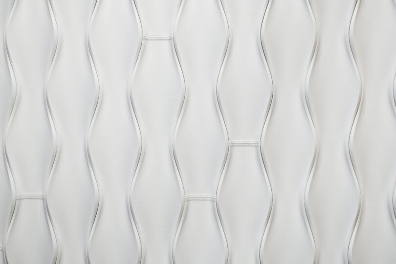 Close-up of a white textured surface, Design 406 by Erwin Hauer, with a wavy, undulating pattern and horizontal stitching at intervals.