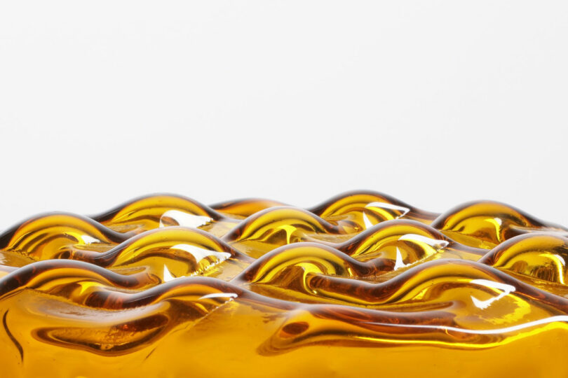 Close-up of an amber-colored glass surface with wavy, undulating patterns.