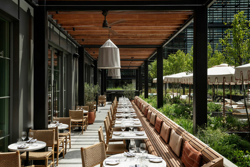 Outdoor dining area with tables and chairs arranged in rows under a wooden pergola at FORTH Hotel. Green plants and parasols can be seen in the background.