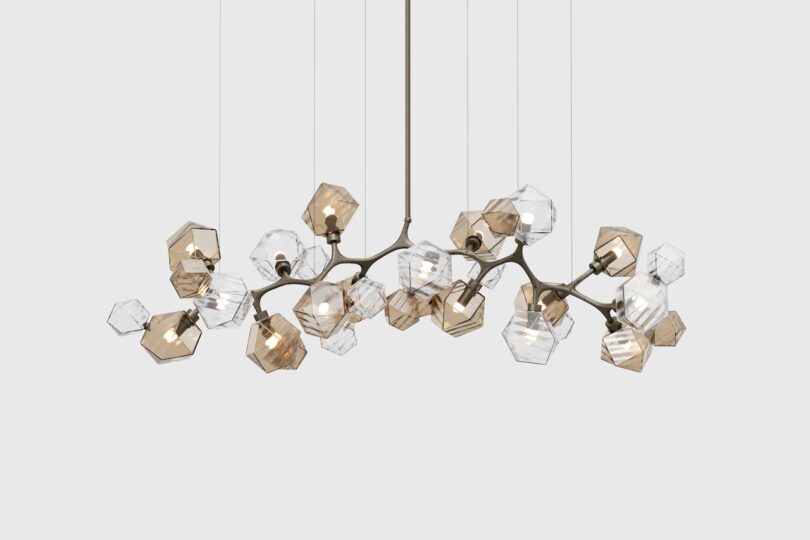 A modern chandelier featuring multiple geometric glass lampshades in clear and amber tones, hanging from a ceiling fixture on thin metal rods