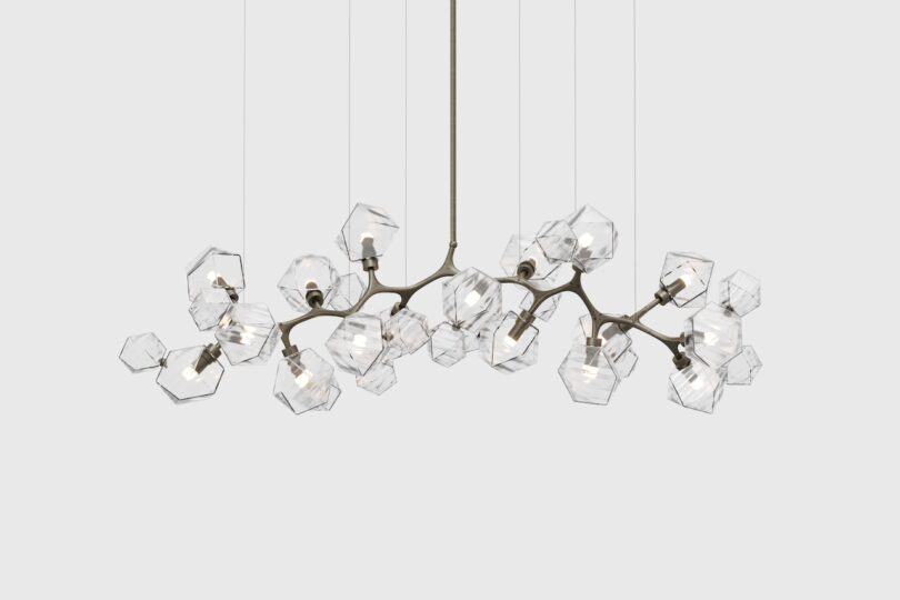 Modern chandelier with multiple hexagonal glass shades on a bronze metal frame, suspended by wires against a plain background.