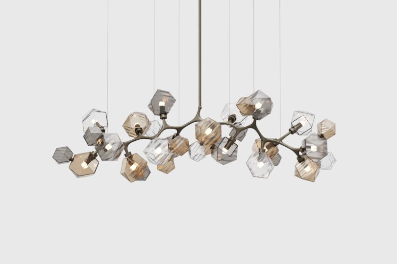 A modern chandelier with multiple geometric glass pendants, some tinted amber and others clear, hanging from thin wires