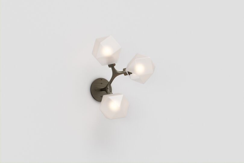 Wall-mounted light fixture with three white, geometric shades on a metal base