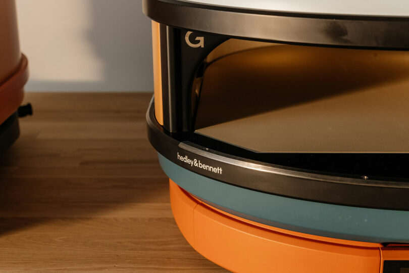 Close-up of a commercial kitchen shelving unit with the Hedley & Bennett logo, showcasing its sturdy metal frame and wooden shelf, placed on a wooden floor.