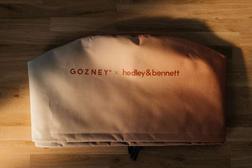 A folded Gozney x Hedley & Bennett branded fabric cover sits on a wooden surface.