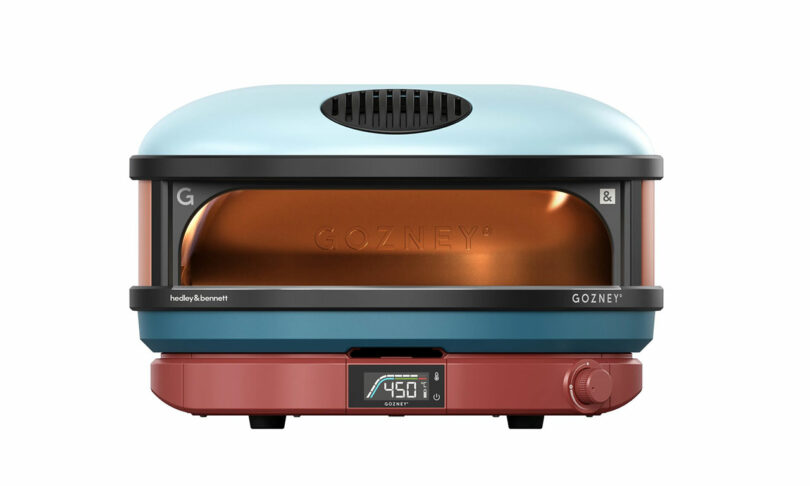 A modern pizza oven with a blue upper half, red base, and digital temperature display set to 450°F. The brand name "Gozney" is visible on the front.