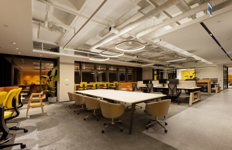 Modern open-plan office with desks, chairs, and overhead lighting. Yellow and black accents dominate the decor.