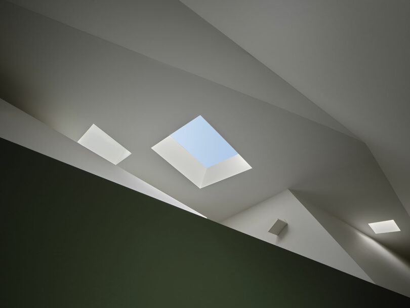 A geometric ceiling design with multiple skylights emits natural light into a modern interior space.