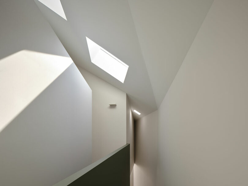 A minimalist interior features inclined white walls with geometric shapes and skylights allowing natural light to enter.