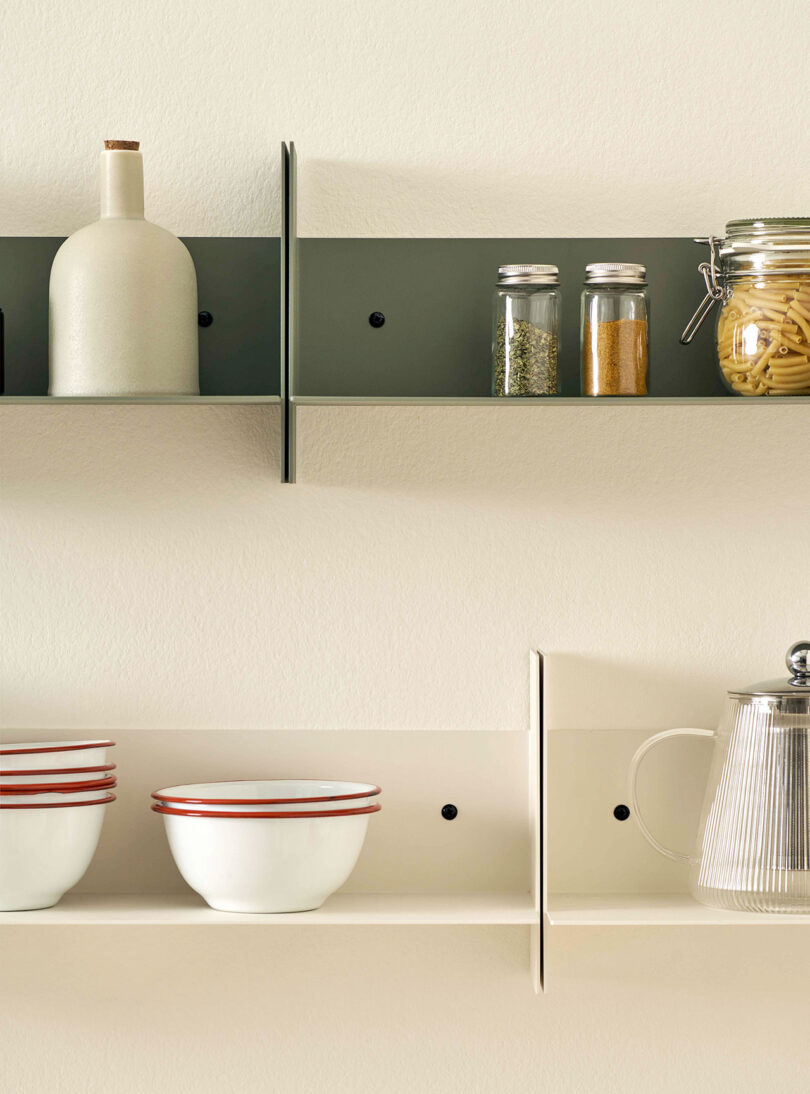 PLI Steel Wall Shelves by TIPTOE holding a ceramic bottle, two jars of spices, pasta in a jar, two bowls, a cup, and a glass coffee pot.