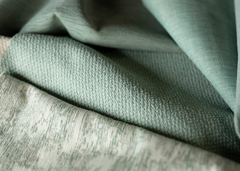 Close-up of overlapping green fabric textures, showcasing different weaves and patterns.