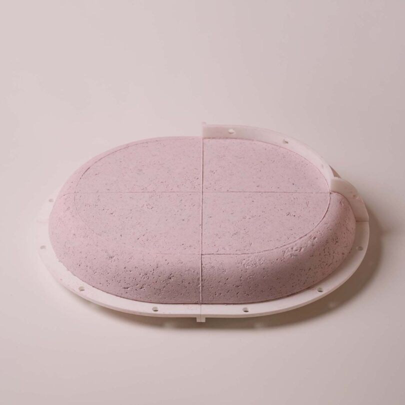 A circular, pink tabletop segmented into four quarters, housed in a white, semi-flexible mold against a neutral background.