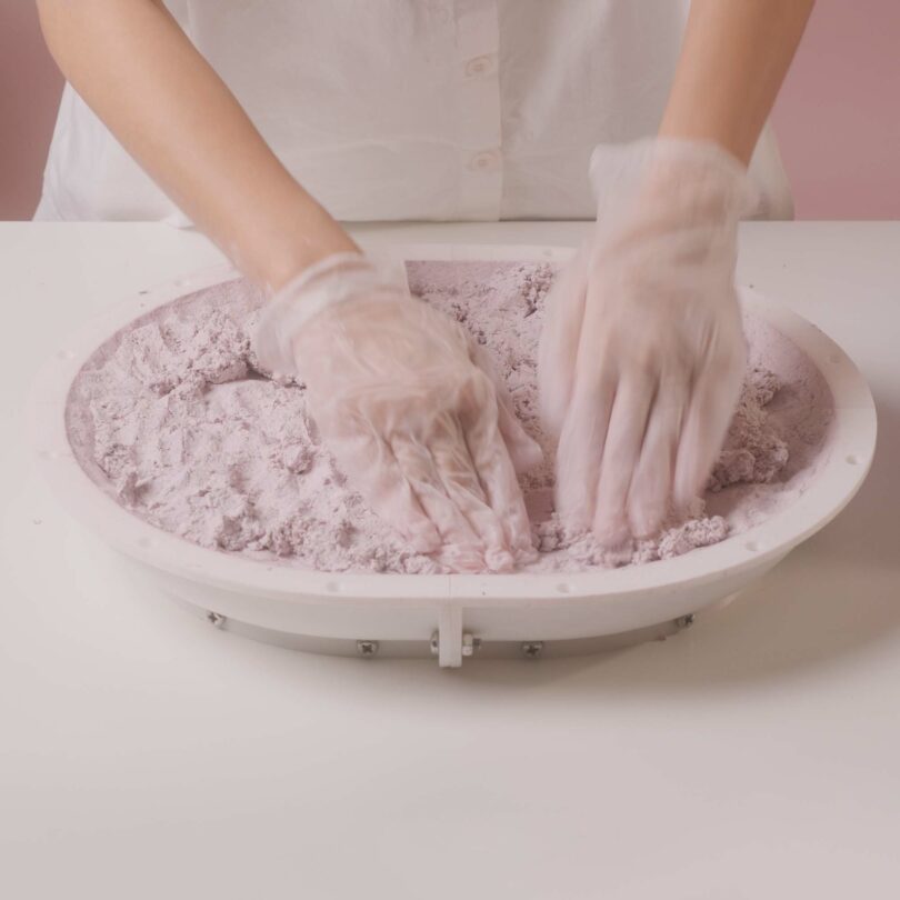 Emeline Ong wearing gloves mixing pink paper composite in a round container on a white surface.