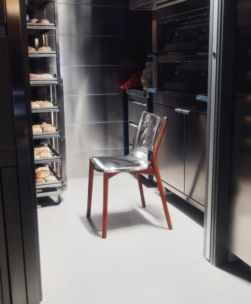 The Poele Chair by Philip Starck and Alessi placed on a light-colored floor in a sleek, modern kitchen. To the left, shelves filled with baked goods are visible.