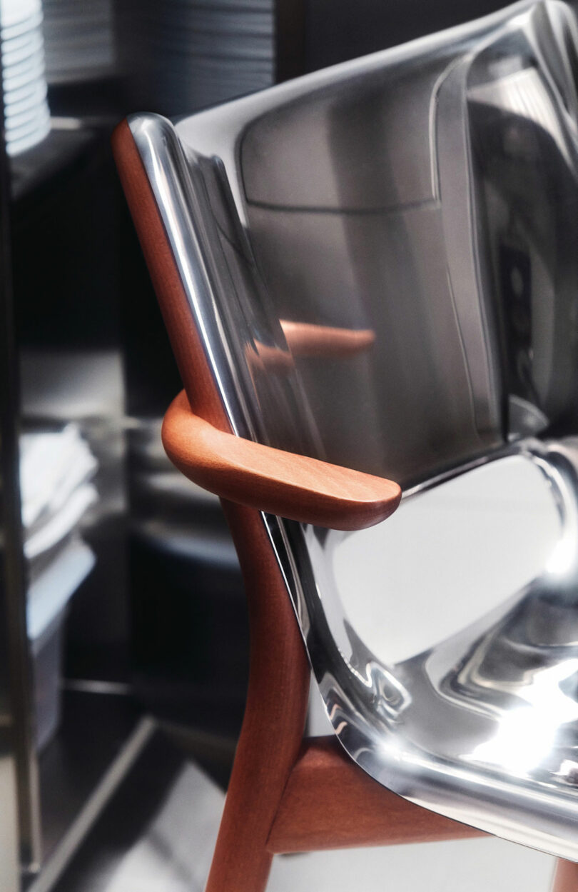 A close-up view of The Poele Chair by Philip Starck and Alessi with a transparent seat and brown wooden arms and legs.