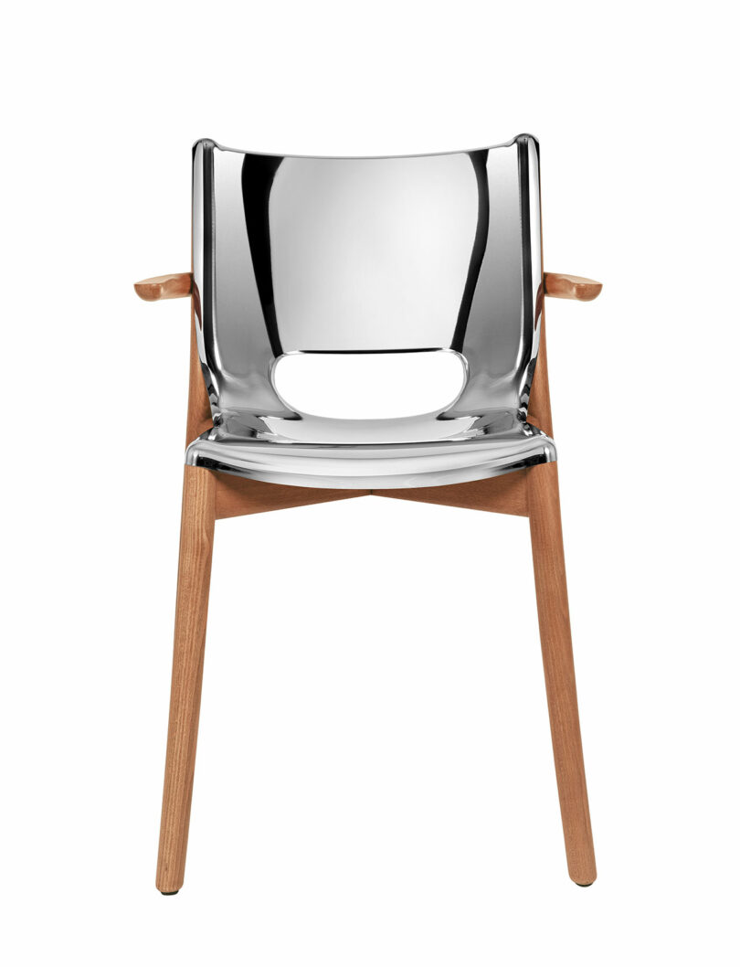 The Poele Chair with a shiny metallic seat and backrest, wooden armrests, and wooden legs.