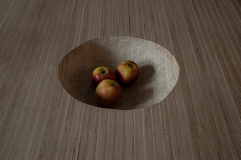 Three apples are placed in a carved circular indent on a wooden surface.