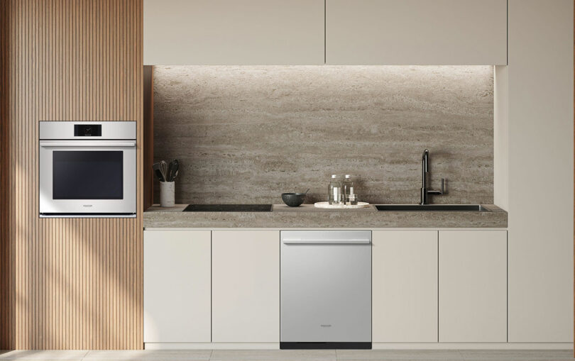 Modern kitchen with stainless steel built-in stove, dishwasher, sink and beige cabinets from the Signature Kitchen Suite. Stone backsplash and worktop with essential kitchen utensils. Vertical wooden slats decorate the left wall.